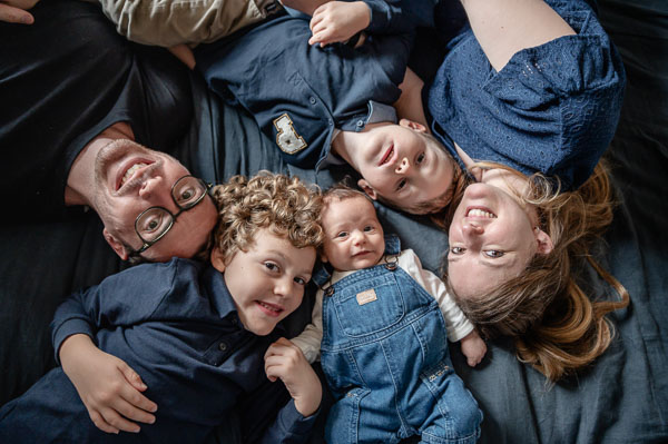 Photo d'une famille au bois d'oingt, les parents et leurs 3 enfants, dont un petit bébé. Ils sont allongés Et regardent l'objectif