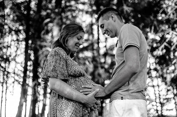 Science photo, grossesse en noir et blanc. D'un couple dans la forêt de sapin Du haut Beaujolais. Le futur papa tient le ventre de la future maman et tous les 2 regardent le ventre arrondi